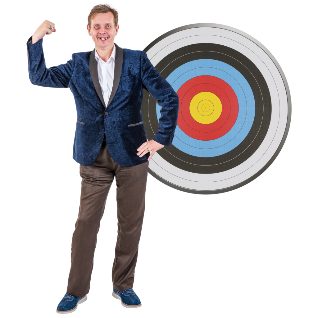 A smiling man in a blue jacket flexing his arm in front of a large archery target.