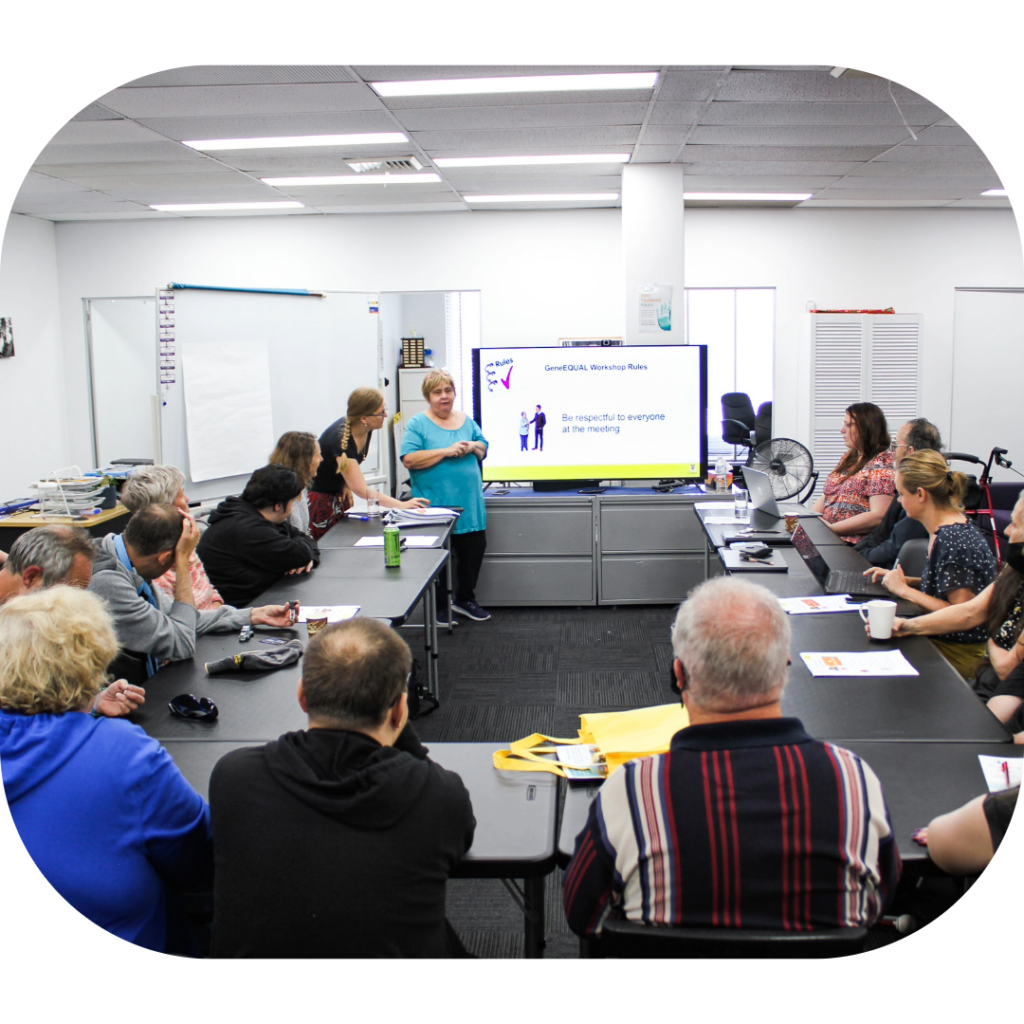 People seated around tables watching a woman speak in front of a presentation screen.