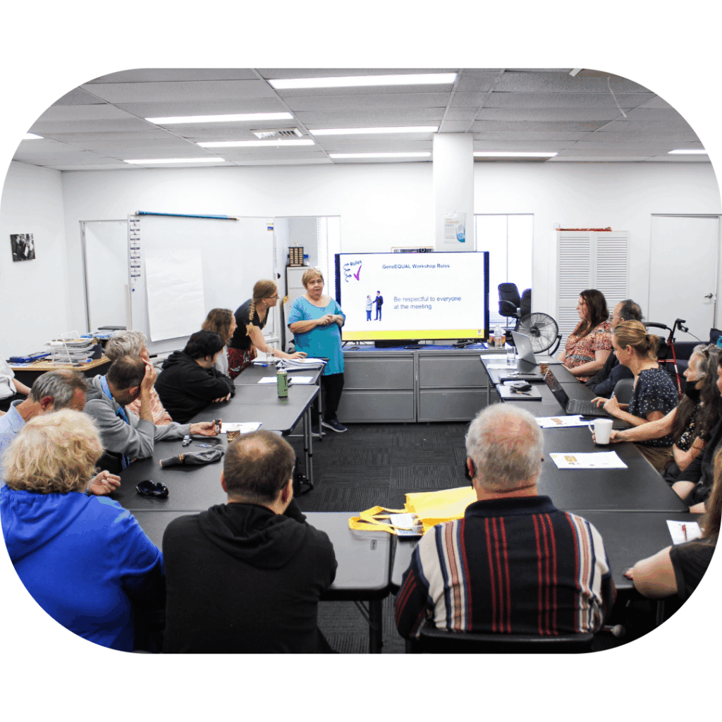 People seated around tables watching a woman speak in front of a presentation screen.